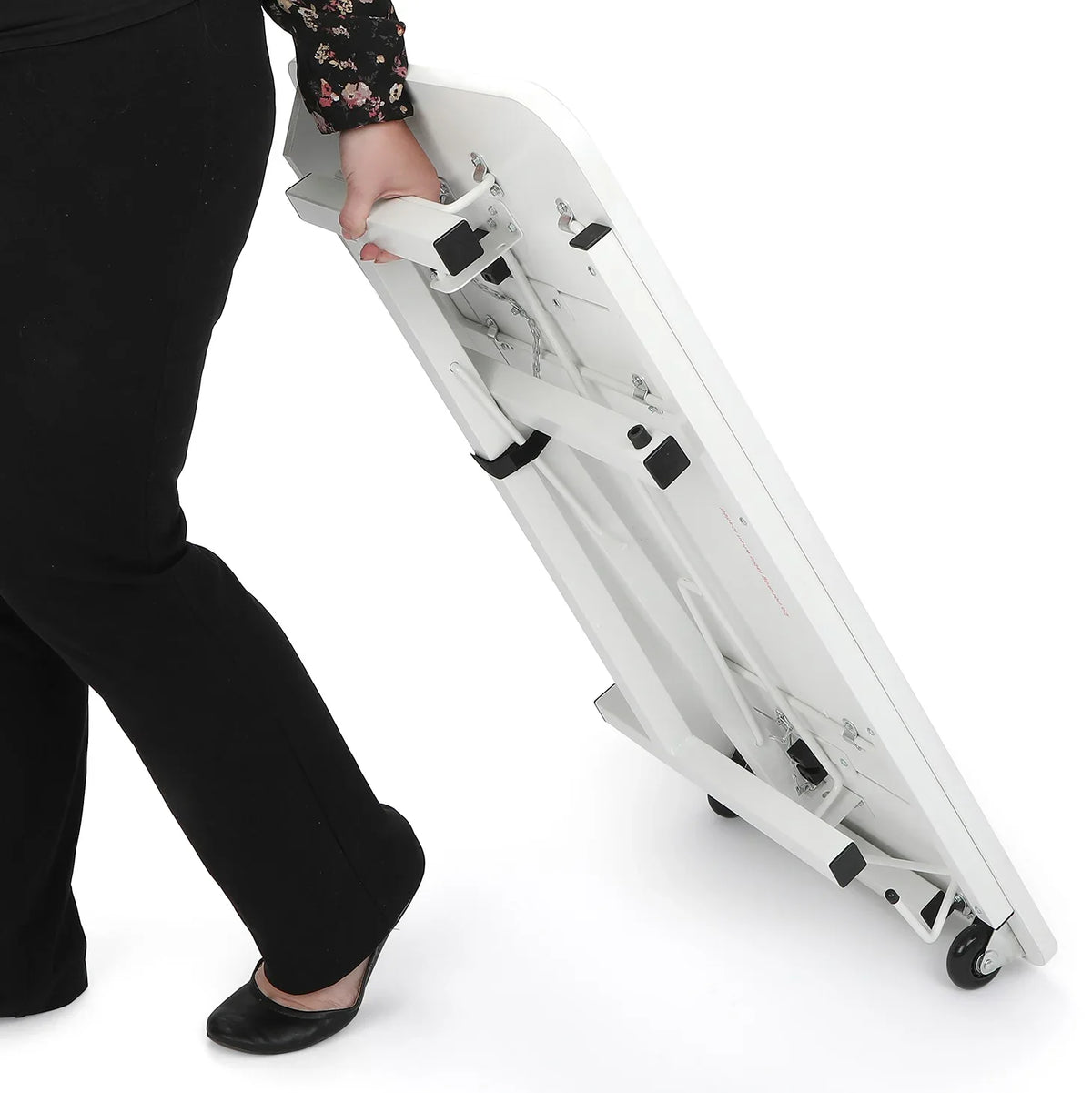 Person transporting the folded Arrow Gidget II Sewing Table 611 using its built-in wheels for mobility.