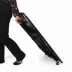 Person rolling and carrying the folded Arrow Heavyweight Sewing Table 611F with built-in caster wheels