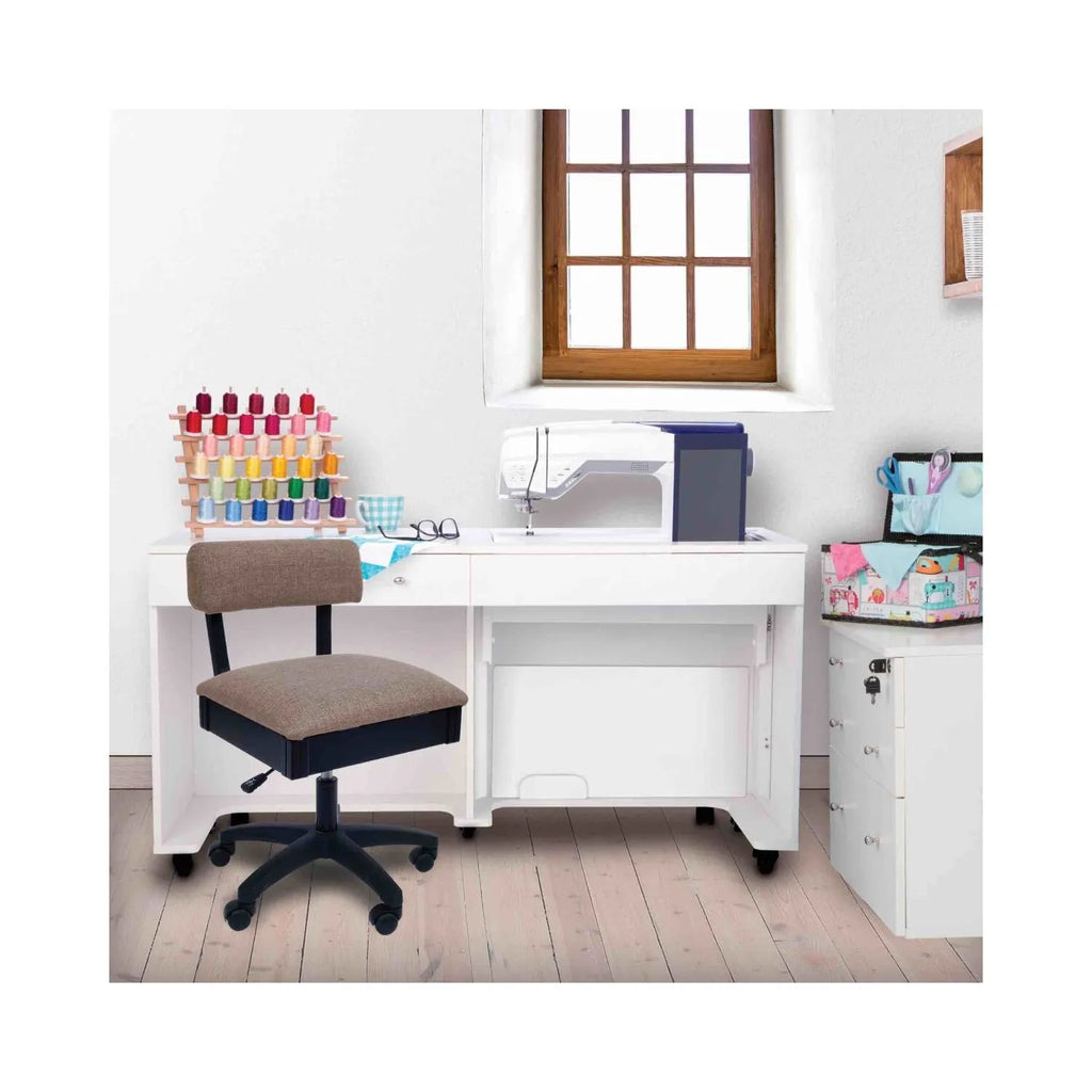 Princess Hazel Hydraulic Sewing Chair in sewing room setup – ergonomic tan swivel chair placed beside white sewing cabinet and machine.