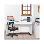 Arrow Black Notions Sewing Chair in crafting room setup – ergonomic swivel chair with sewing-themed fabric placed at white sewing cabinet workstation.