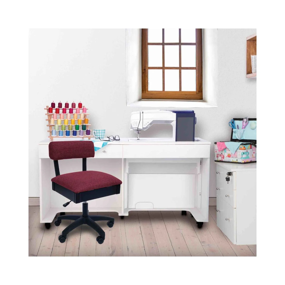 Madame Scarlet Hydraulic Sewing Chair in sewing room setup – ergonomic red swivel chair placed beside white sewing cabinet and machine.