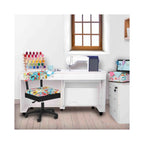 Arrow Sew Wow Hydraulic Sewing Chair in sewing room setup – colorful sewing-pattern chair paired with white sewing cabinet, machine, and crafting tools.