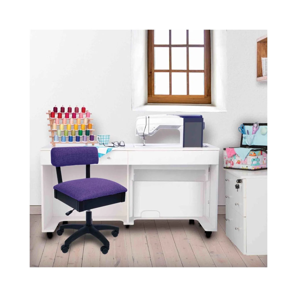 Royal Purple Hydraulic Sewing Chair in sewing room setup – ergonomic purple swivel chair paired with white sewing cabinet and machine.