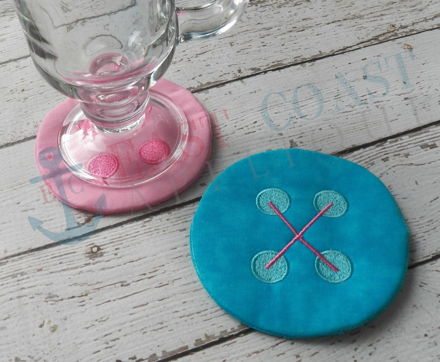 Pink and turquoise embroidered button coasters shown with a glass