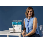 Woman sitting next to a white and blue sewing machine on a table with a blue background