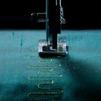 Sewing machine needle stitching on teal fabric