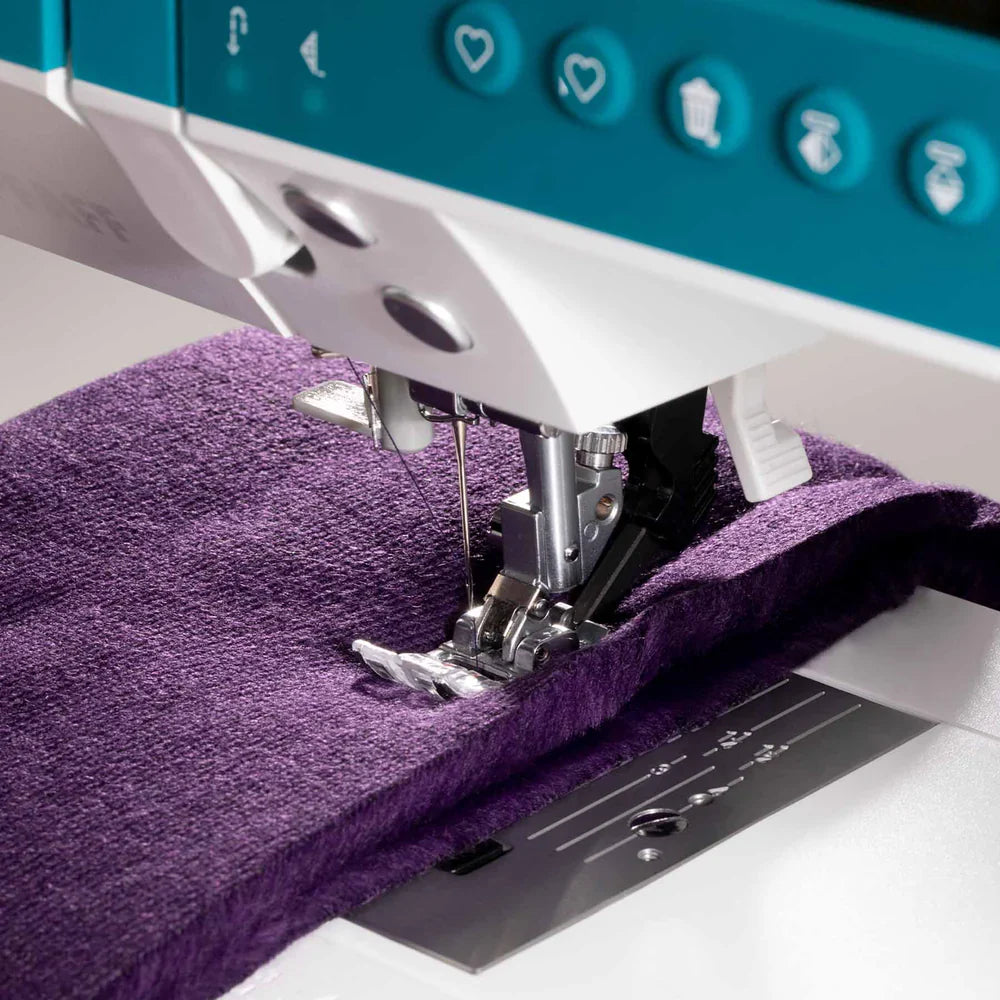 Sewing machine stitching purple fabric on a white background