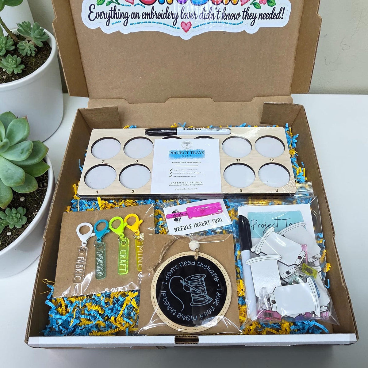 Gift box contents with numbered project trays, project tags, needle tool, scissor fobs, and ornament