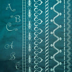 Teal fabric with white embroidery patterns including letters, leaves, and abstract designs.