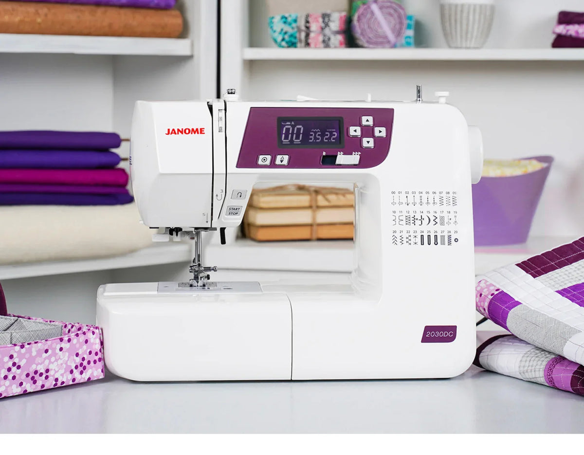 Janome 2030DC-G sewing machine displayed in a sewing room setting with quilting projects and fabrics.