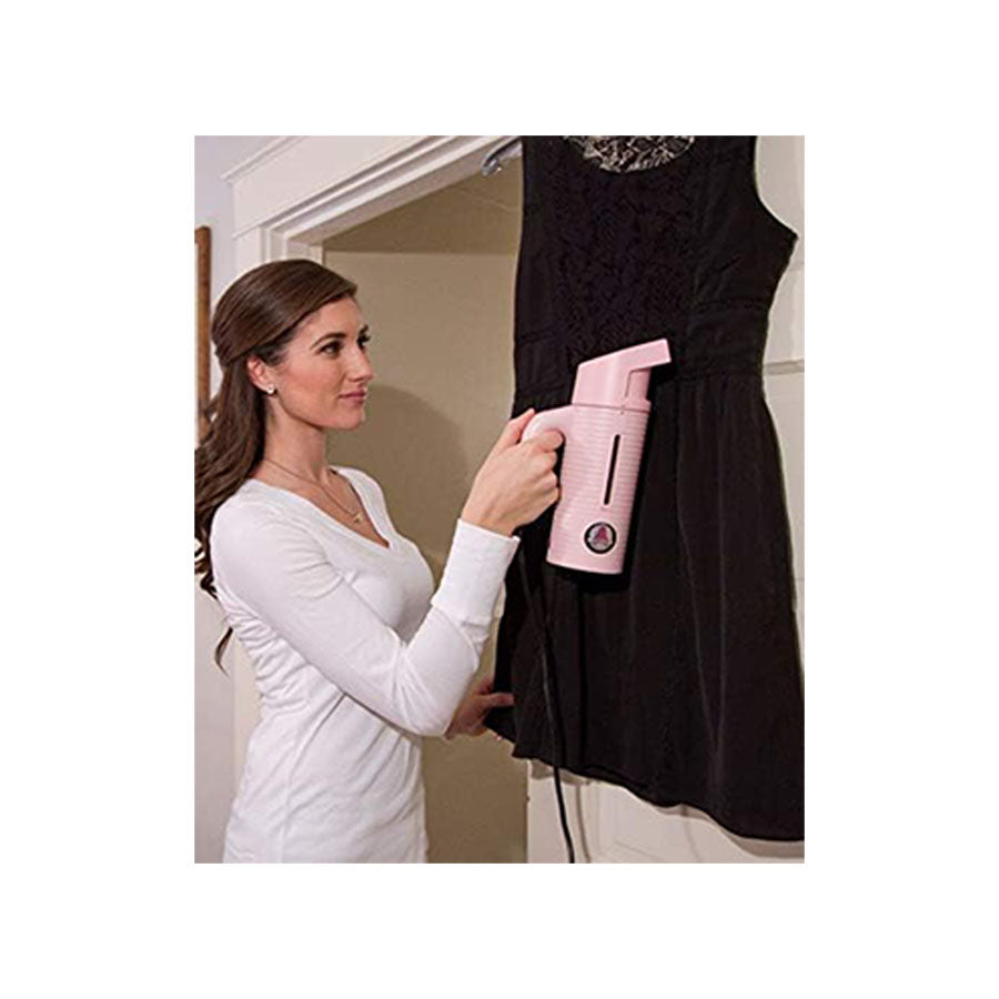 Woman using the Jiffy ESTEAM Pink Travel Steamer to remove wrinkles from a dress, demonstrating handheld garment steaming at home.