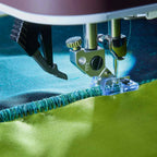 Close-up of a sewing machine needle stitching green fabric.