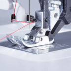 Close-up of a sewing machine needle and foot with red thread on a light gray background