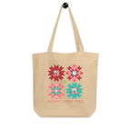 Front of the Cozy Cheer tote hanging by its straps, with red, pink and teal quilt stars and Merry Christmas lettering.