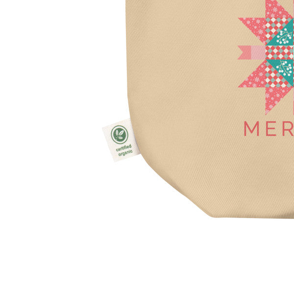 Close-up of the Cozy Cheer tote's woven fabric, pink-and-teal quilt-star print and certified-organic side label.