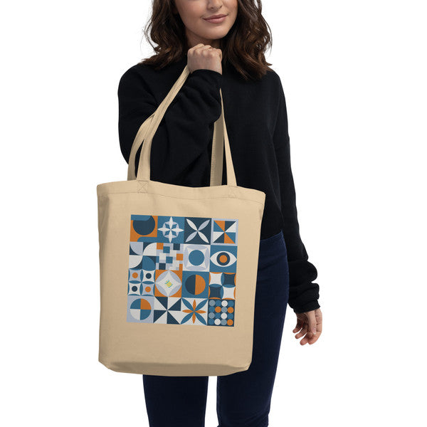 Model carrying a natural-color tote with retro geometric quilt blocks in blue, rust and cream.