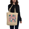 Model carrying a natural-color tote with retro geometric quilt blocks in coral, forest green and cream.