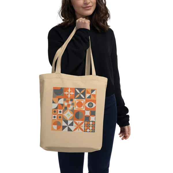 Model carrying a natural-color tote with retro geometric quilt blocks in gray, orange and cream.