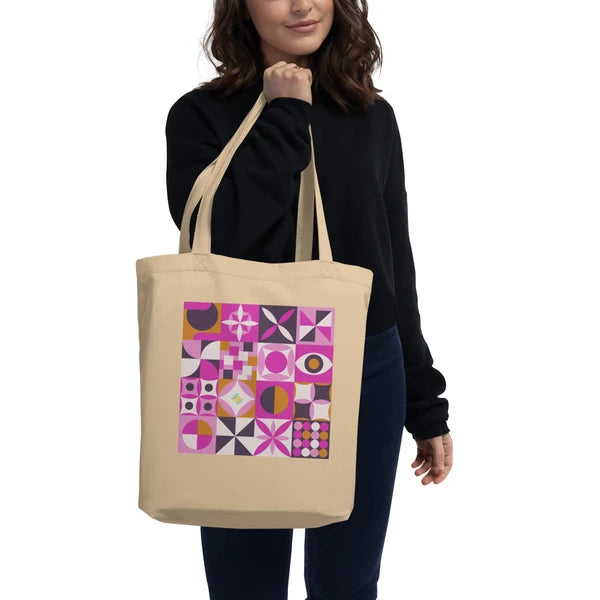 Model carrying a natural-color tote with retro geometric quilt blocks in pink, plum and cream.
