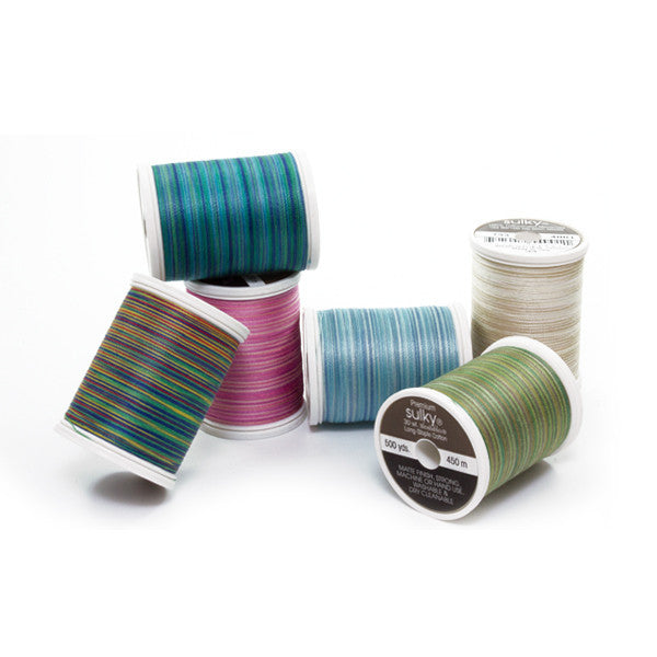 Six Sulky Cotton Blendables spools in teal, pink, blue, cream, green and rainbow shades, stacked and resting on their sides.