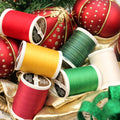 Red, yellow, green, cream and variegated Sulky thread spools displayed among red-and-gold Christmas ornaments.