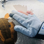 Hands wearing Swan Amity quilting gloves guide an appliqué quilt under a sewing machine, with exposed fingertips visible.