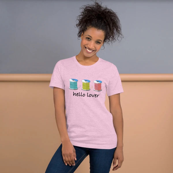 Model wearing the Heather Prism Lilac Hello Lover T-shirt with three colorful thread spools above black script lettering.
