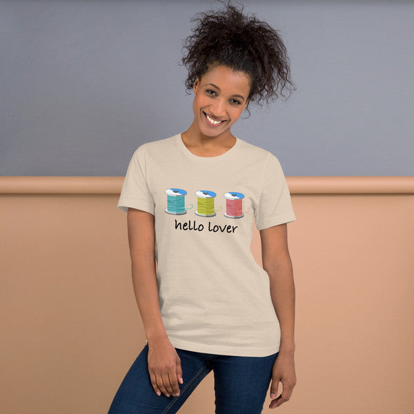 Model wearing the Soft Cream Hello Lover T-shirt with three colorful thread spools above black script lettering.