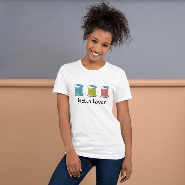 Model wearing the White Hello Lover T-shirt with three colorful thread spools above black script lettering.