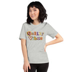 Model wearing the Athletic Heather Quilty Vibes T-shirt with multicolored retro lettering across the chest.