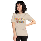 Model wearing the Soft Cream Quilty Vibes T-shirt with multicolored retro lettering across the chest.