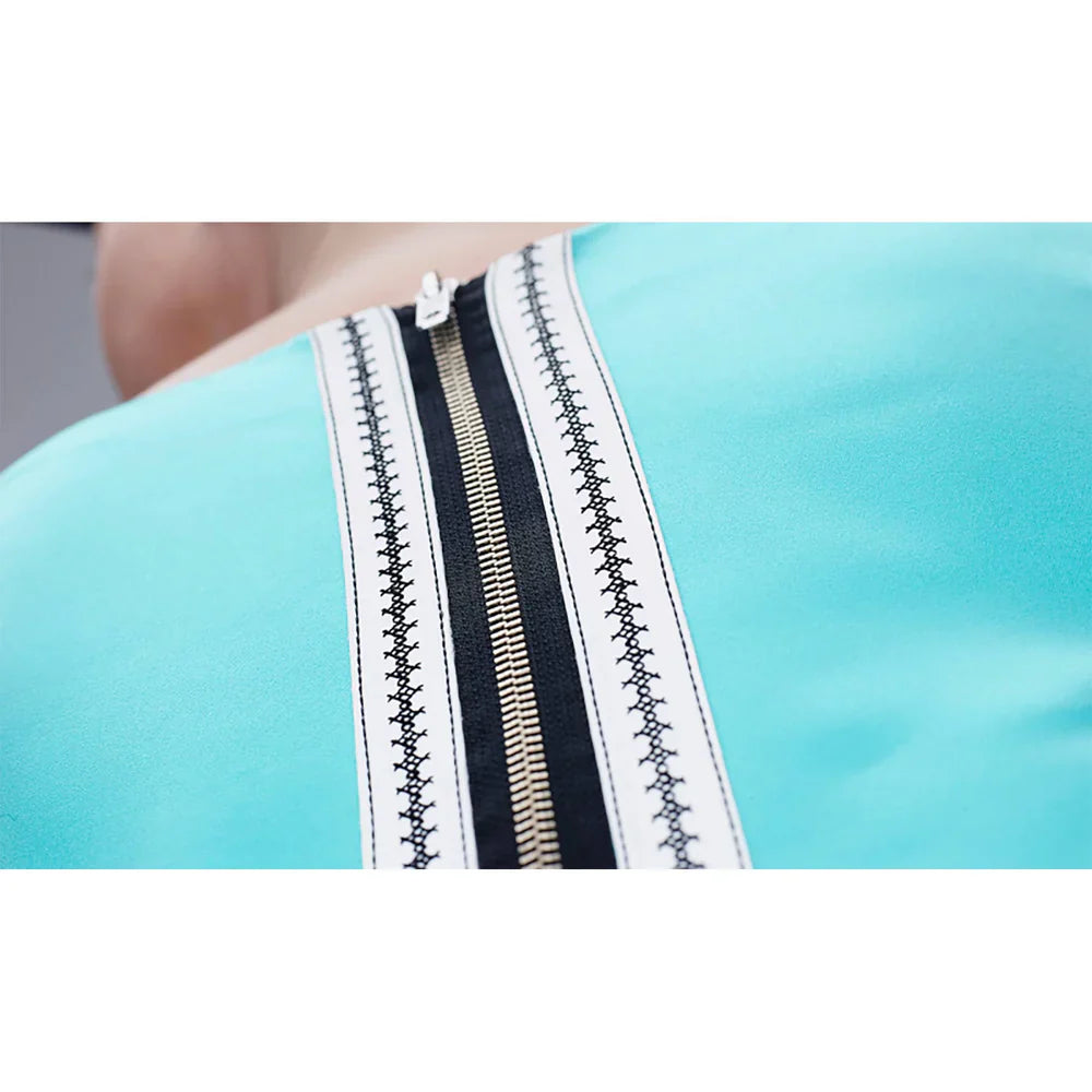 Close-up of a turquoise garment with decorative zippers and stitching.