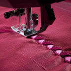 Sewing machine needle stitching a pattern on red fabric