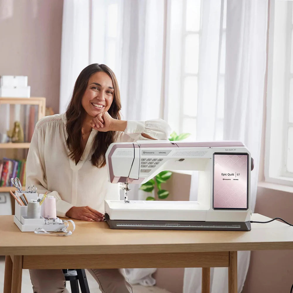 Quilter using the Husqvarna Viking EPIC QUILT 97 sewing machine on a tabletop in a bright home sewing studio