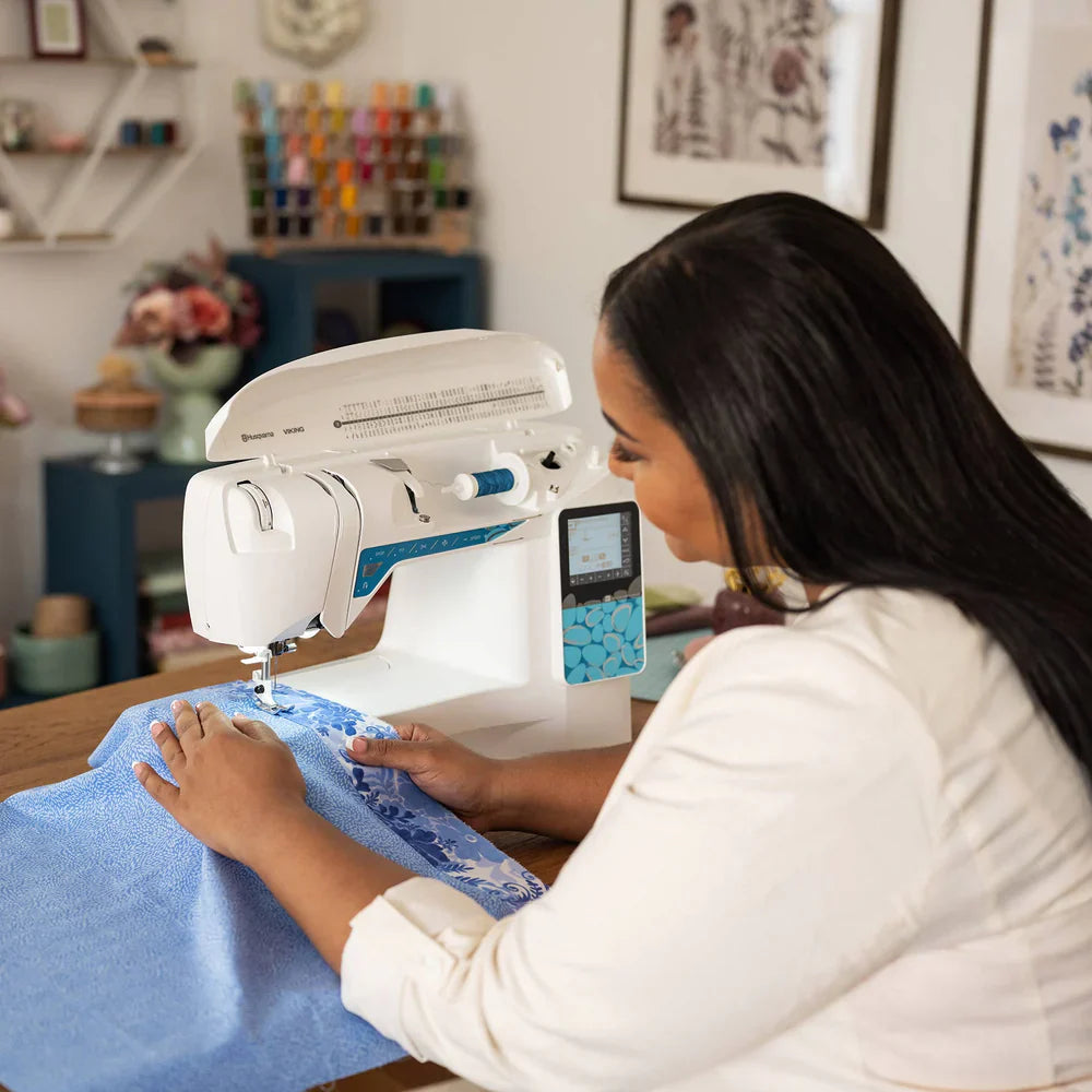 Husqvarna Viking Opal 670 sewing machine in use by sewist stitching fabric on a wooden table in a home sewing studio