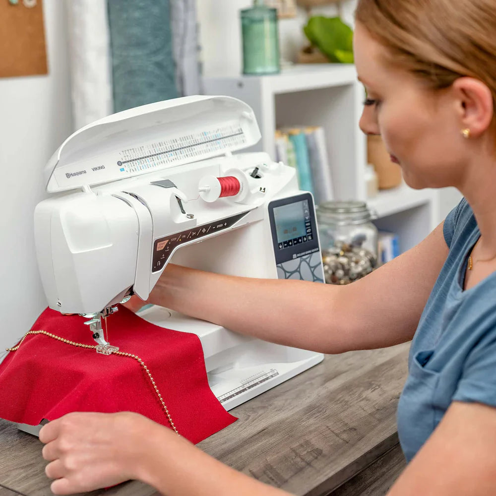 Husqvarna Viking Opal 690Q sewing machine stitching red fabric with decorative trim using precision feed system