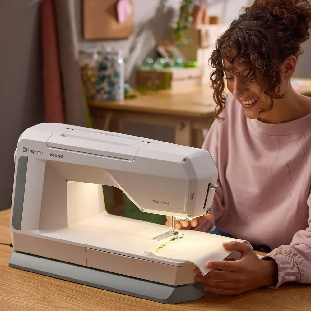 Sewist using Husqvarna Viking Topaz 55Q sewing machine for creative home sewing project in modern workspace