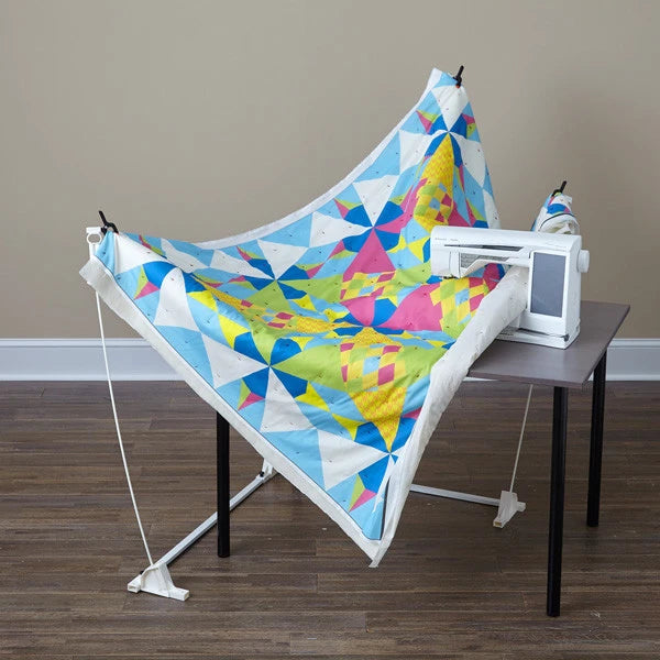 DIME Weightless Quilter frame lifting a bright geometric quilt around a sewing machine on a table.