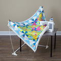 DIME Weightless Quilter frame lifting a bright geometric quilt around a sewing machine on a table.