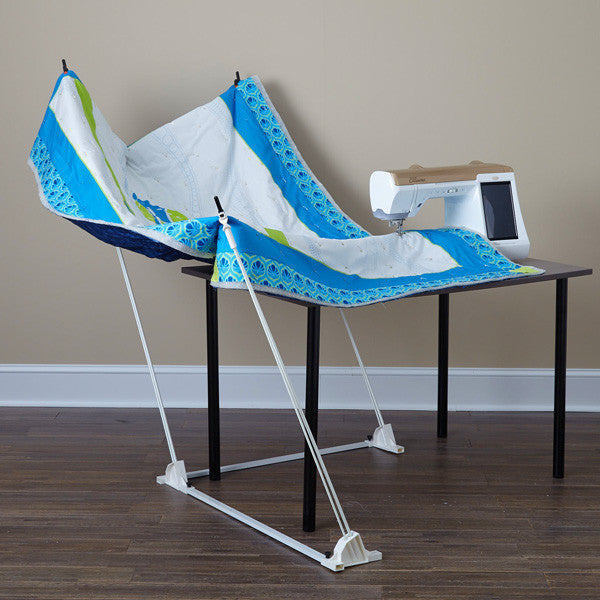 Weightless Quilter support poles suspending a blue-and-white quilt around a tabletop sewing machine.